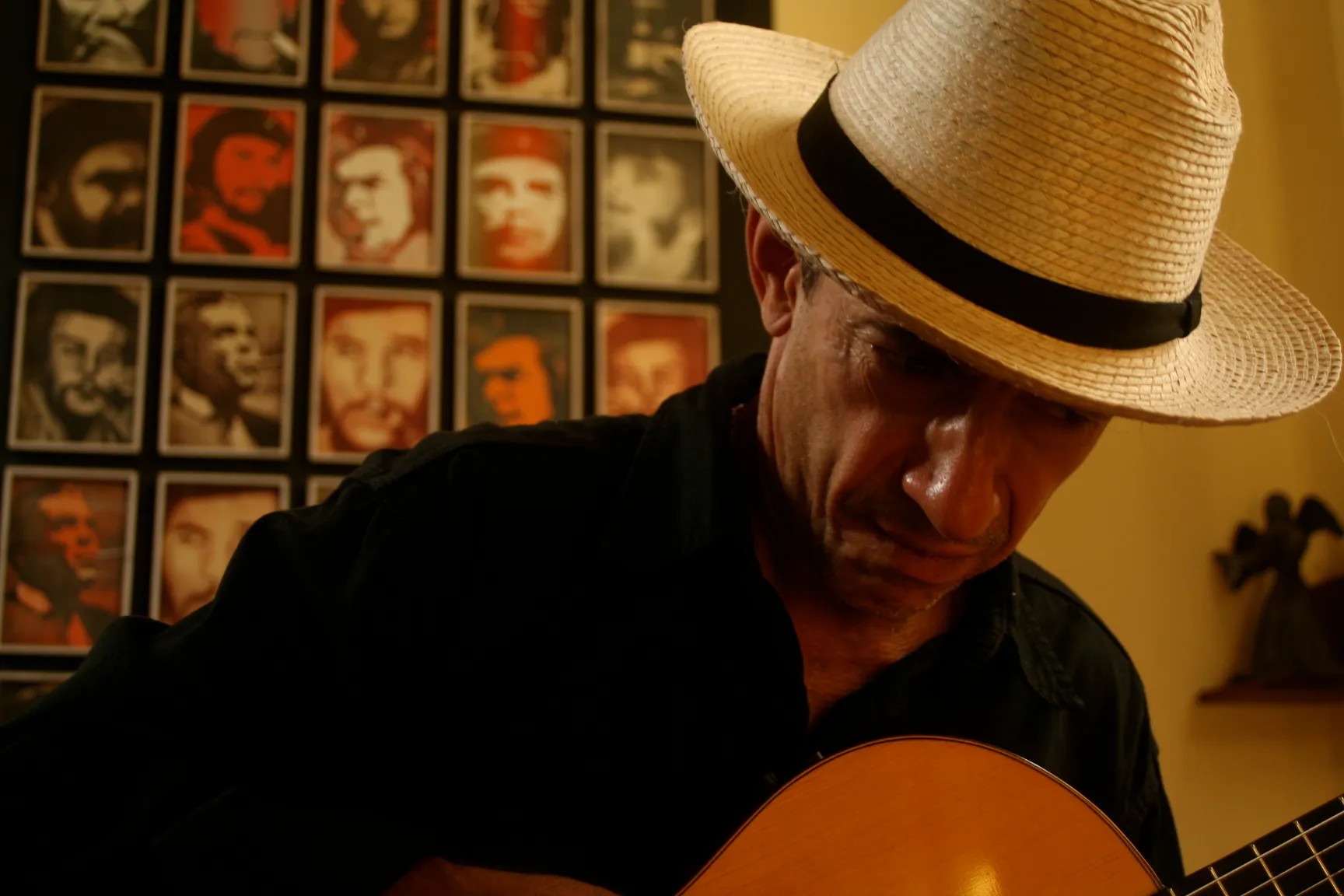 Pablo Lopez-Nussa, chapeau de paille, jouant de la guitare devant un mur de portraits